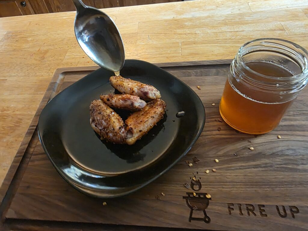 Spoonful of hot honey over smoked wings next to an open jar of hot honey