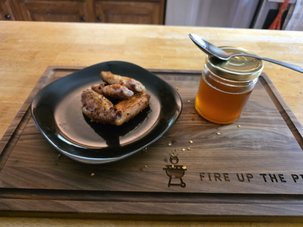 Smoked chicken wings with a jar of homemade hot honey on a Fire Up The Pit cutting board