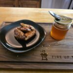 Homemade Hot Honey (Sweet Heat for Wings, Pizza & More) Smoked chicken wings with a jar of homemade hot honey on a Fire Up The Pit cutting board
