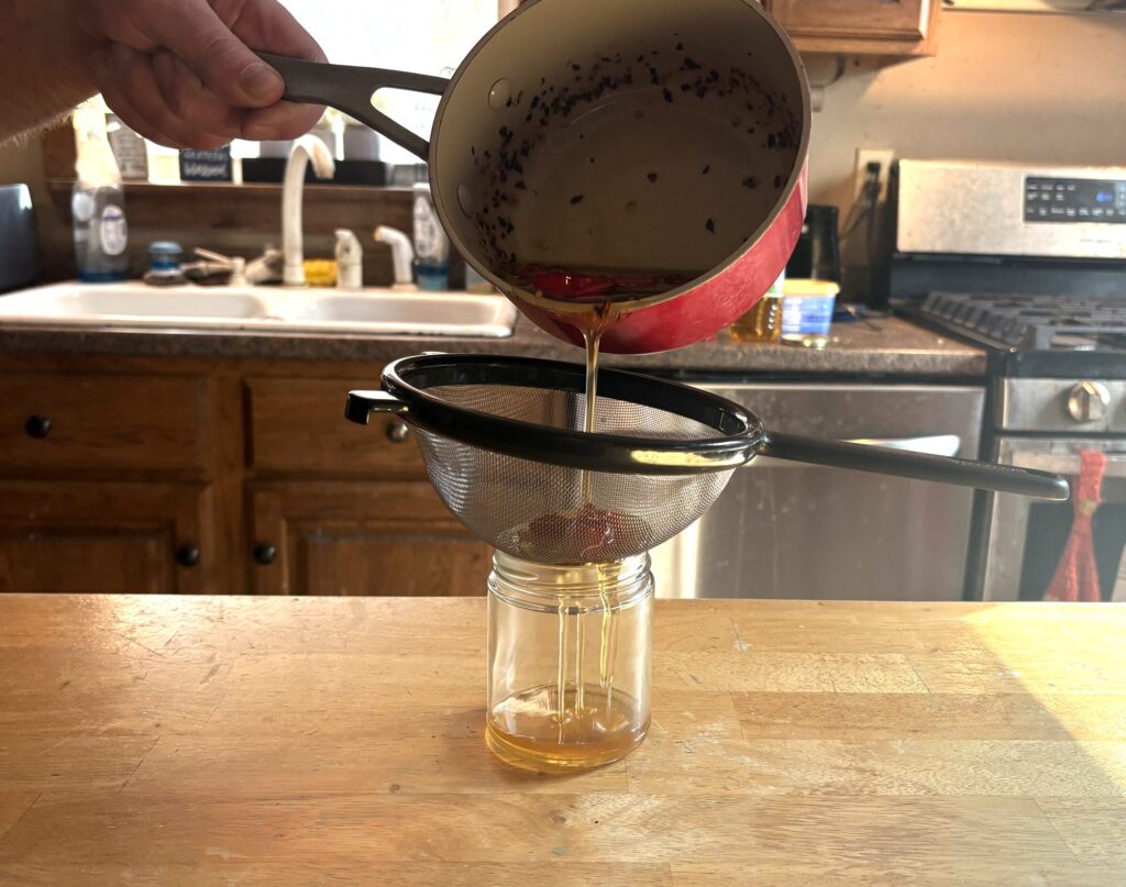 Pouring hot honey through a fine mesh strainer into a glass jar